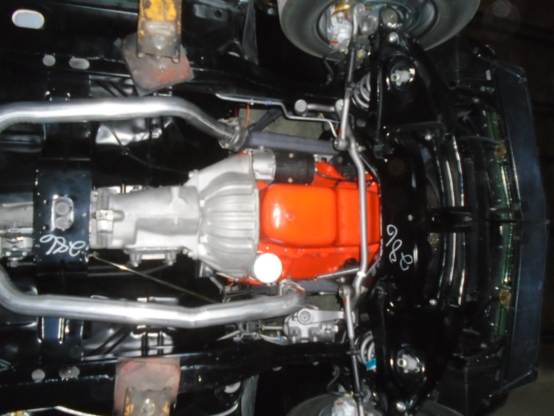 Underside view of a black car with an orange engine and silver exhaust pipes.