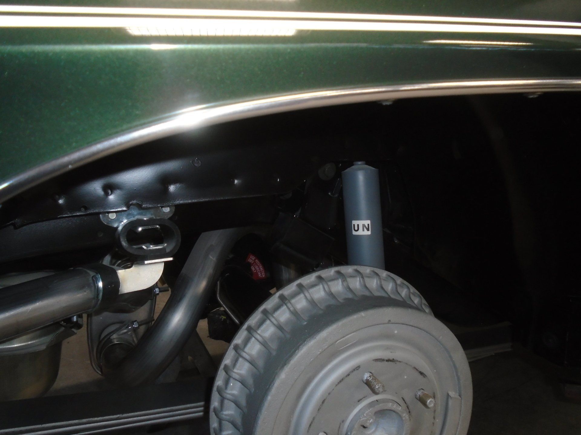 Black and green classic car wheel well with a tire, shock, and exhaust pipe visible.