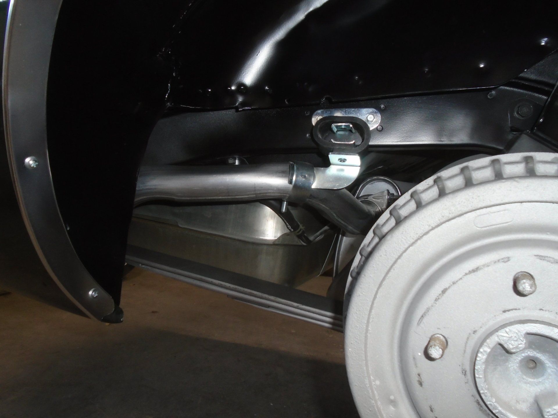 Black car's rear wheel, exhaust pipe, and support bracket visible.