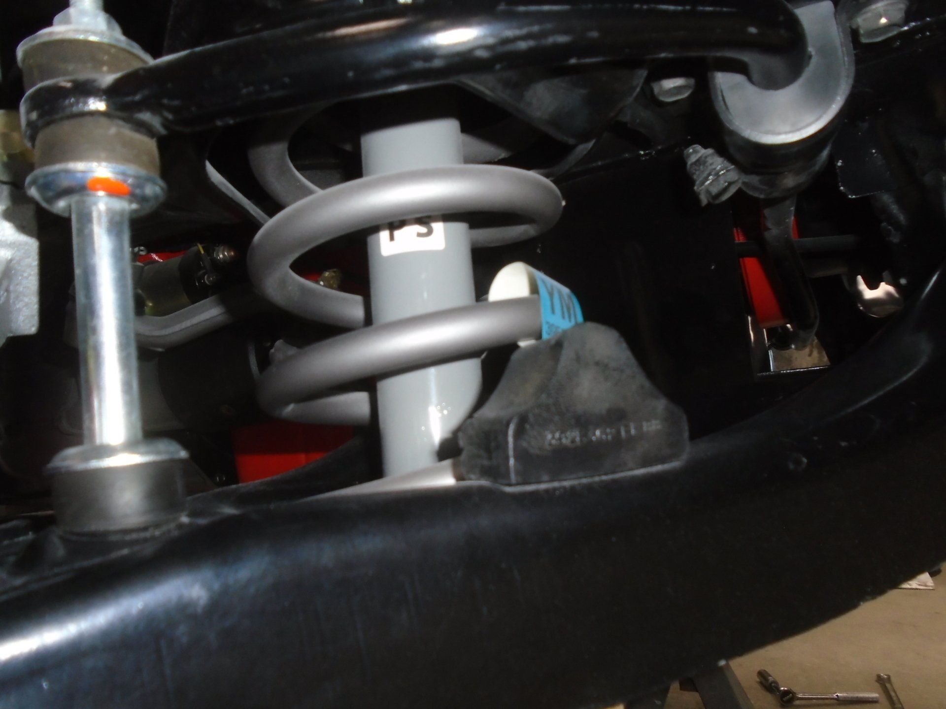 Close-up of car suspension with a gray coil spring and shock absorber; black frame.
