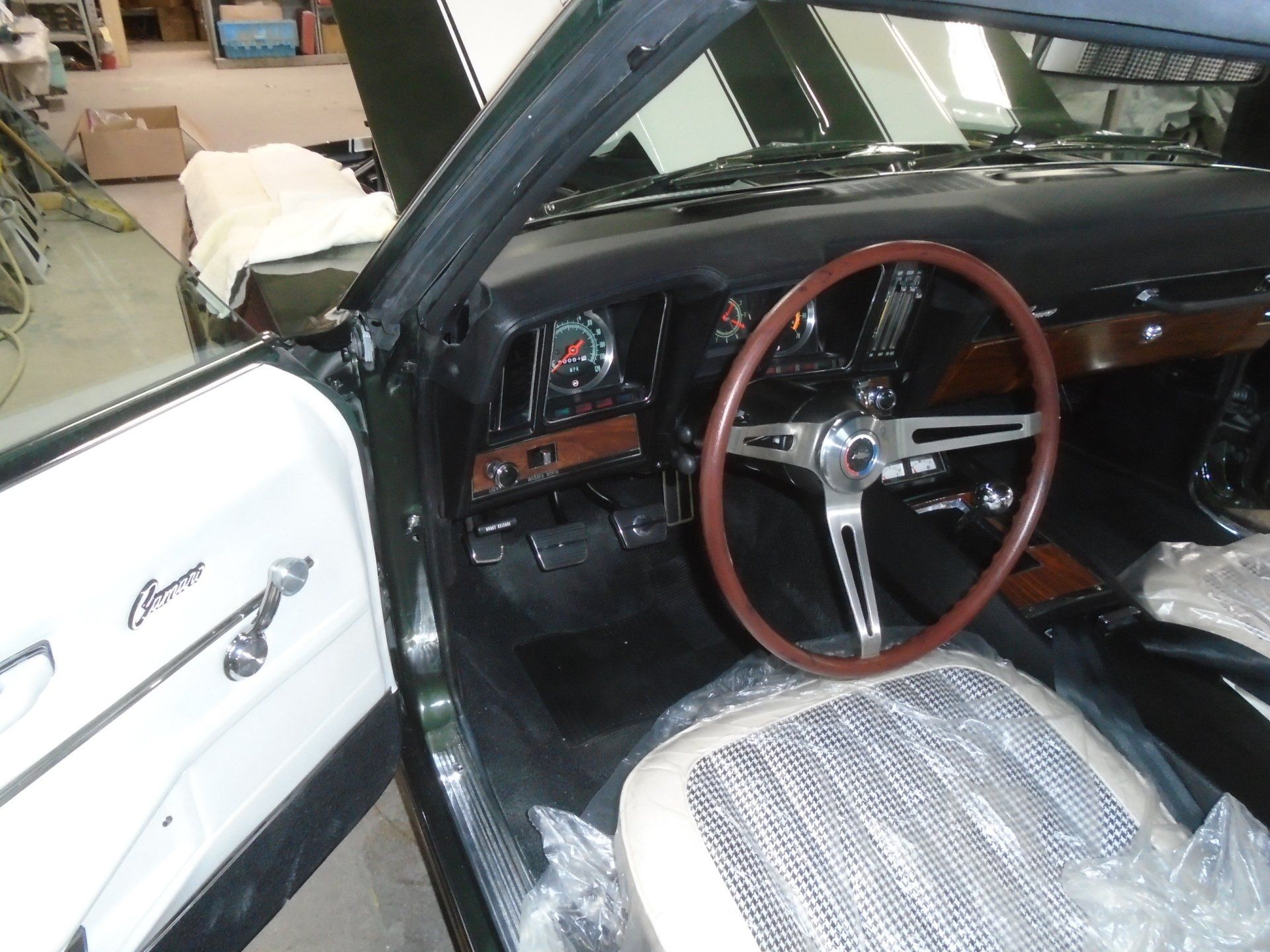 Interior of a classic green car: dashboard, wood steering wheel, white door panel, and a covered seat.