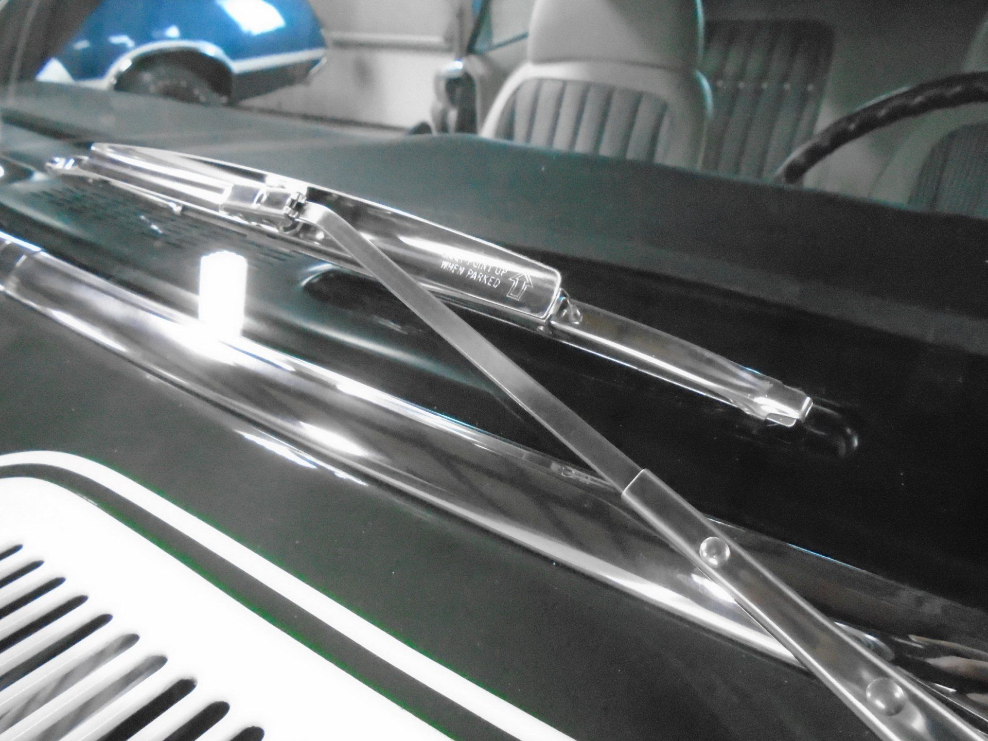 Close-up of classic car's windshield with chrome wiper blades, showing the interior. The car is black.