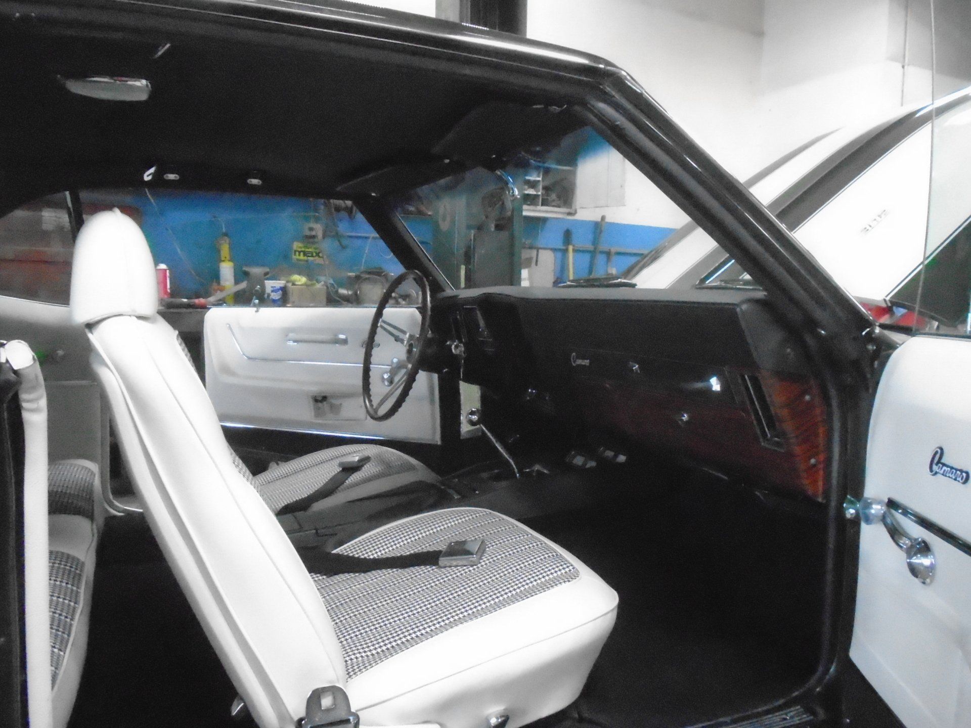 Interior view of a white and black classic car with white seats, black dashboard, and a steering wheel.