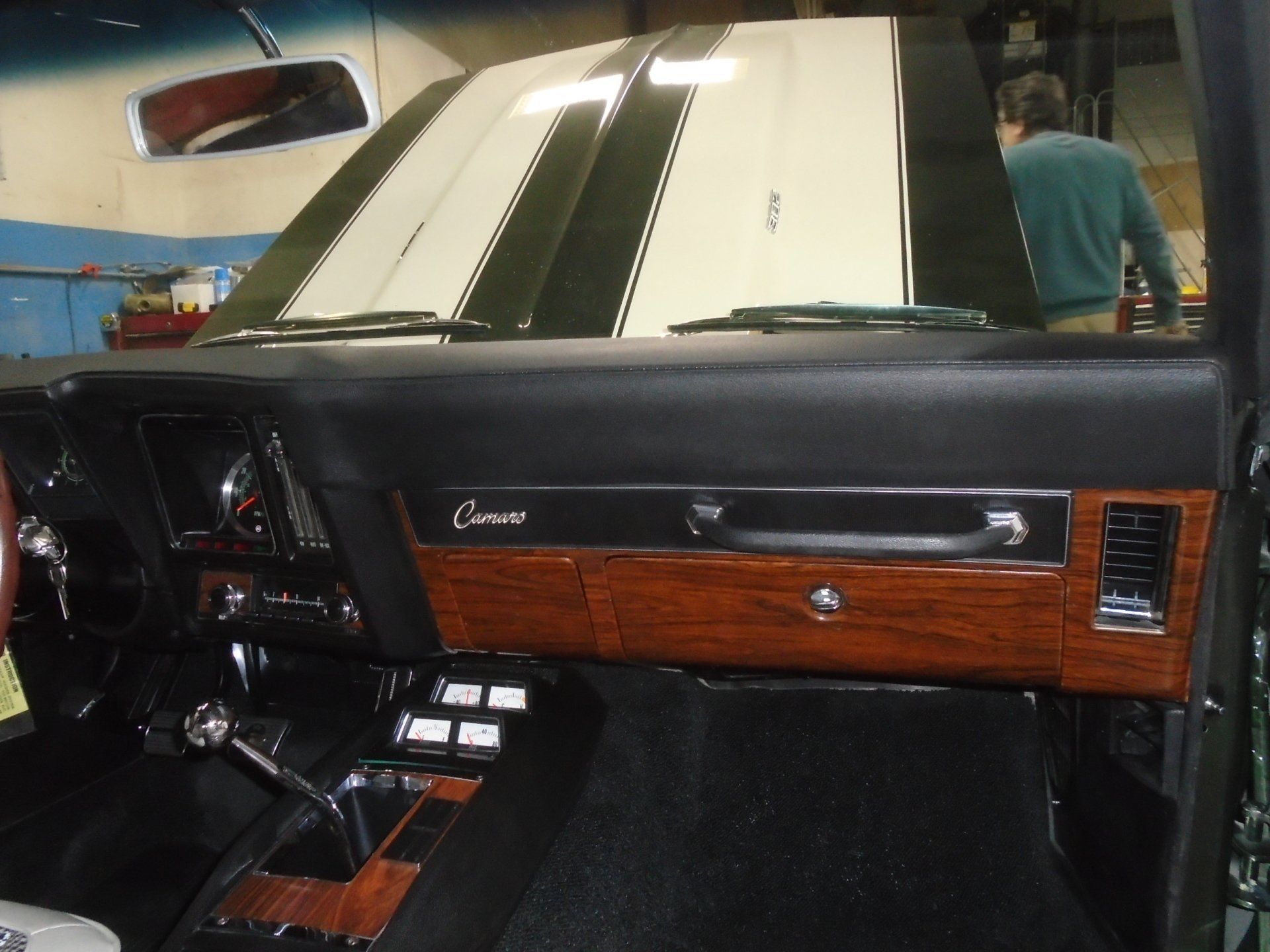 Interior of a classic Camaro with woodgrain trim, black dashboard, and white and green stripes on the hood.
