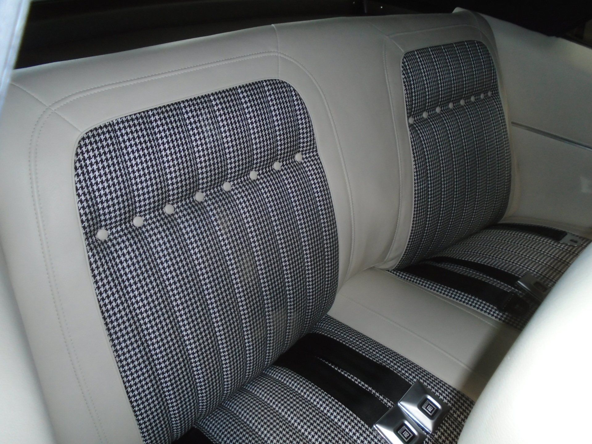 Cream-colored car rear seat with houndstooth patterned center sections and silver-colored seat belts.