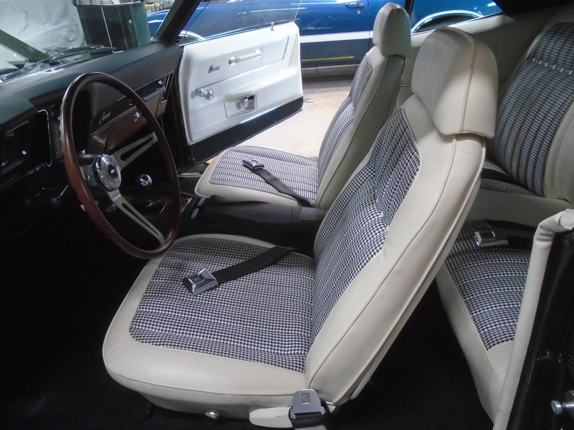 Interior of a classic car with cream seats and patterned fabric inserts, black steering wheel.