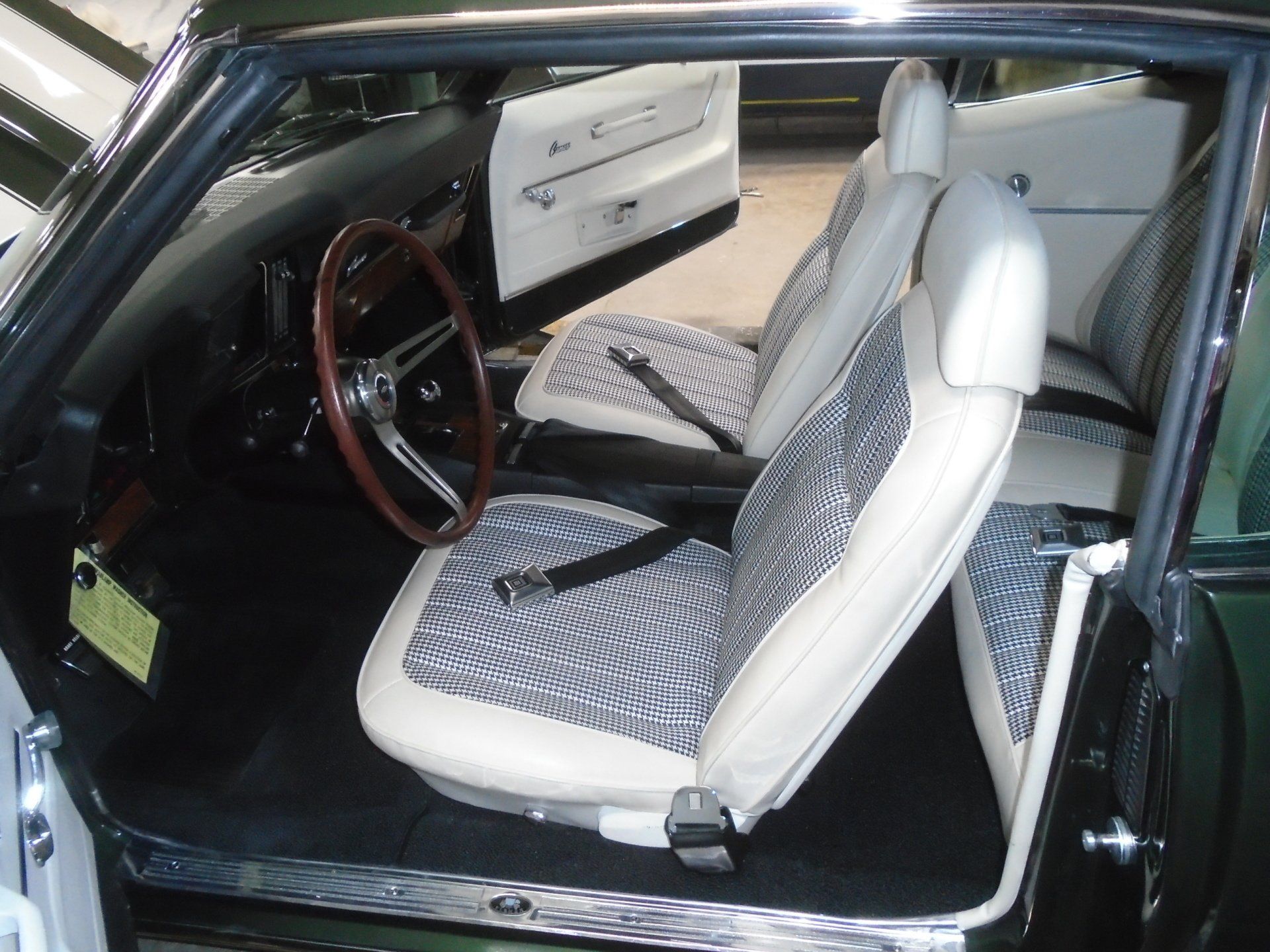 Interior of a classic green car with white and patterned seats, black dash, and a wooden steering wheel.