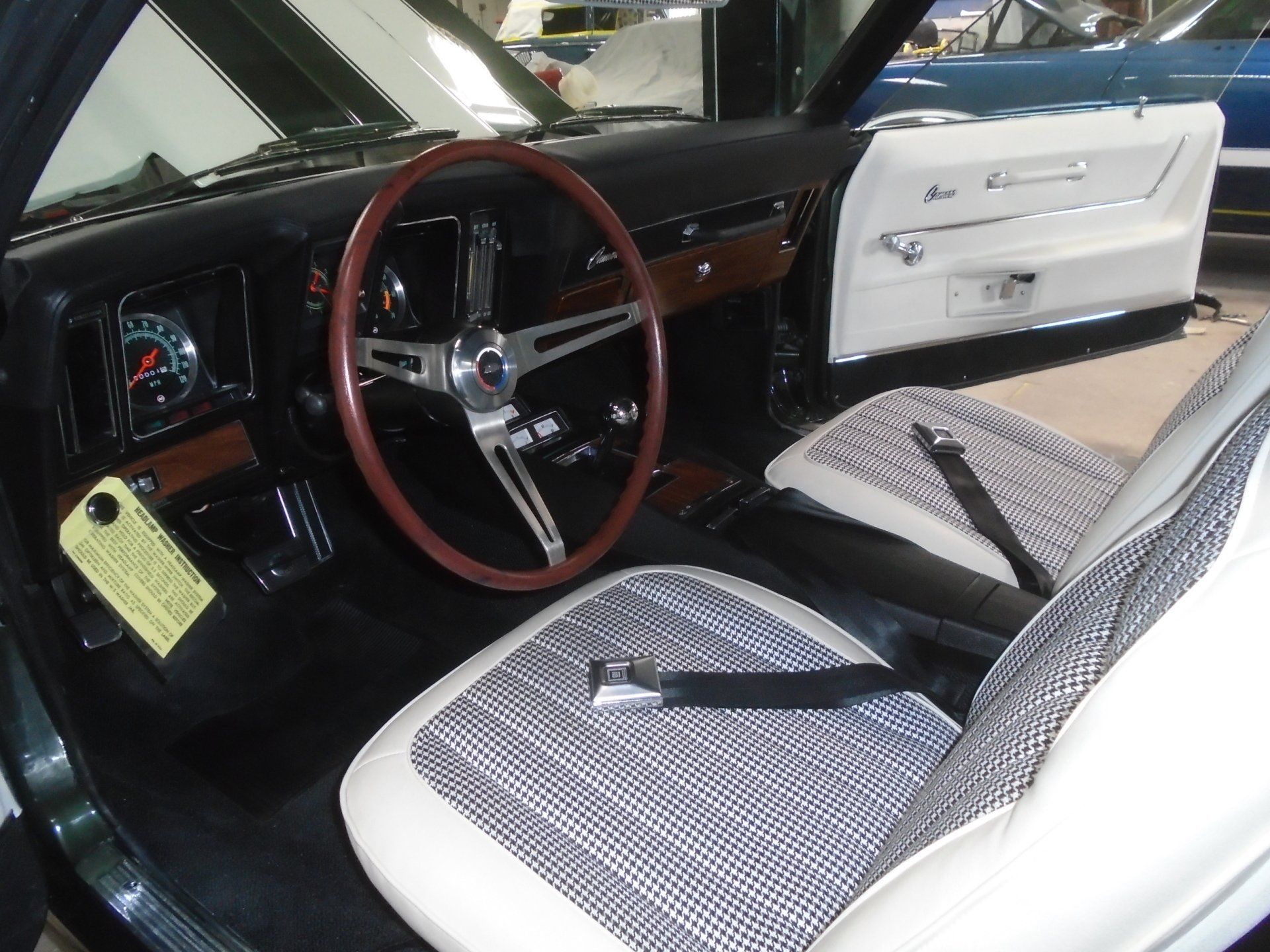Black and white interior of a classic car, featuring a wooden steering wheel and houndstooth seats.