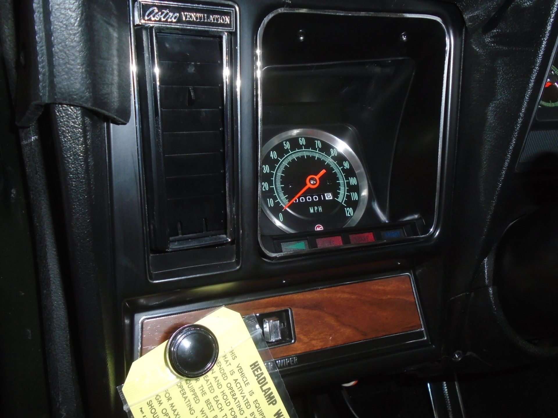 Dashboard of a classic black car with a speedometer, wooden trim, and air vent.
