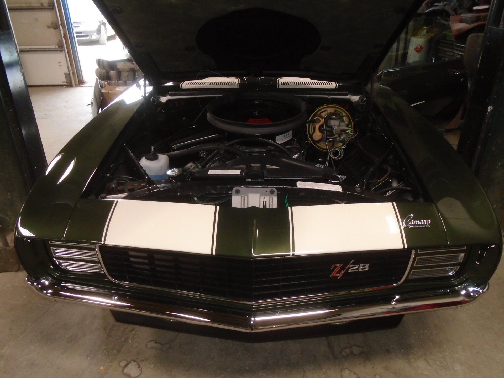 Dark green classic Chevrolet Camaro Z/28 with white stripes, hood open, engine bay visible.
