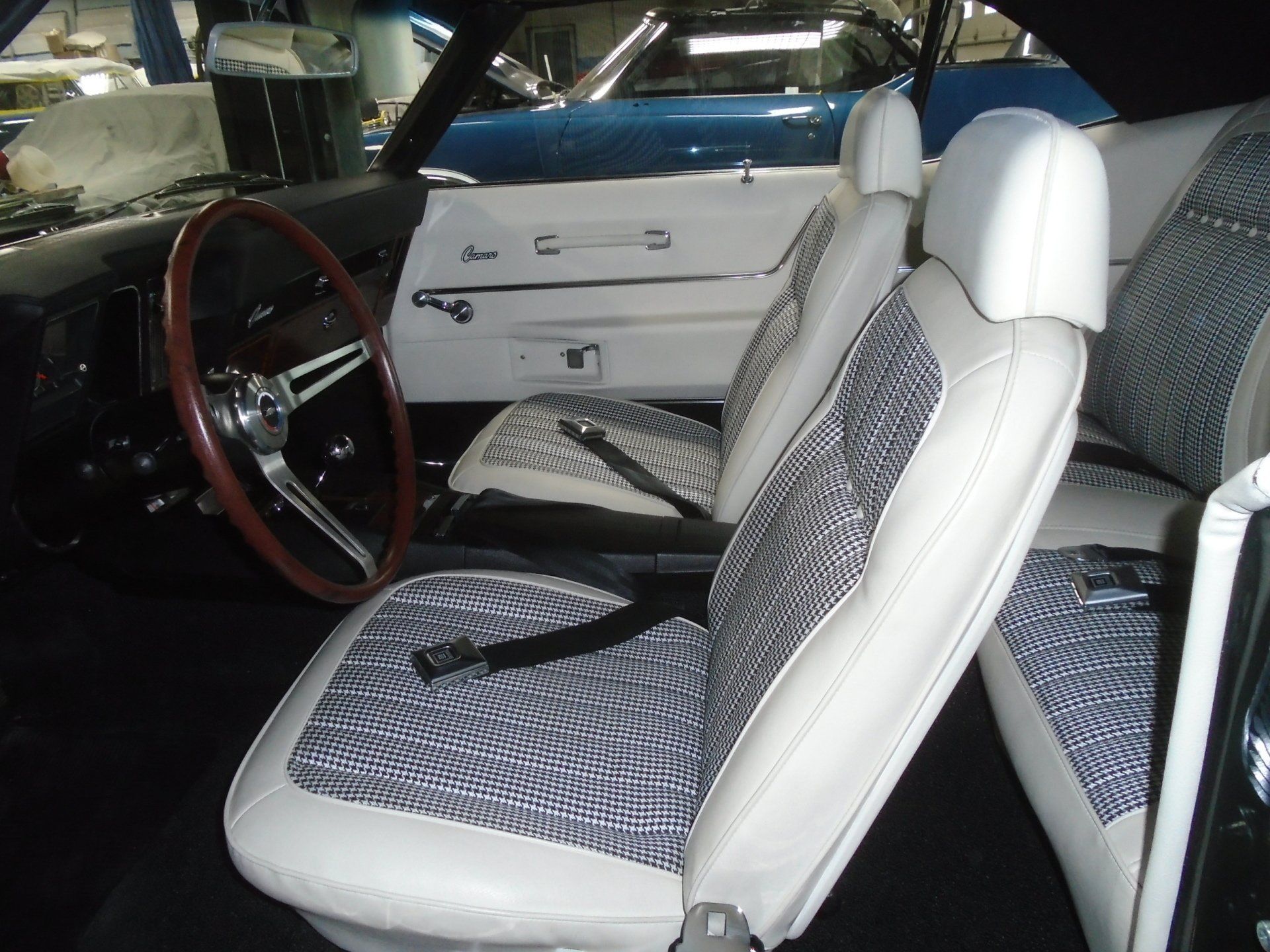 White and patterned car seats in black interior, wood steering wheel.