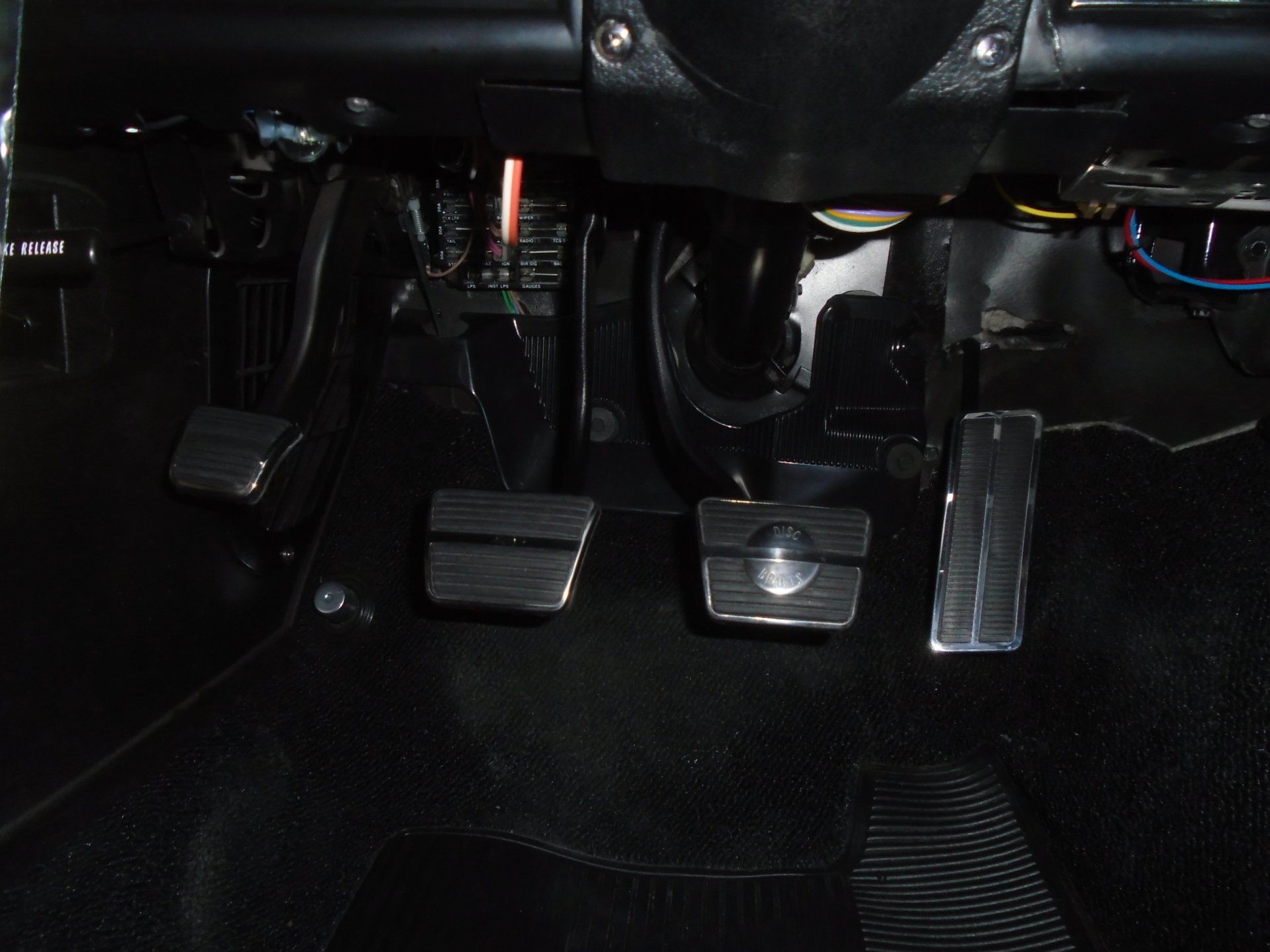 Car pedals: brake, gas, and clutch, made of metal, against a black background.