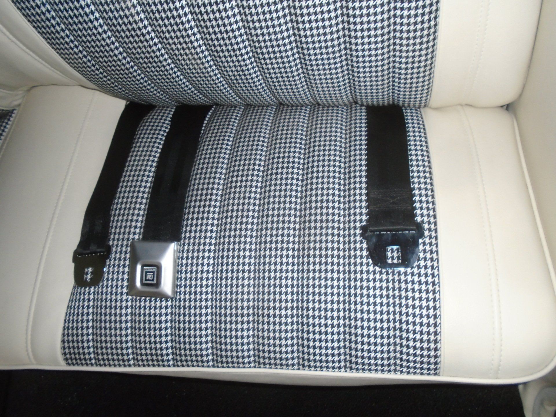 Back seat with houndstooth center, cream sides, and three black seatbelts buckled.