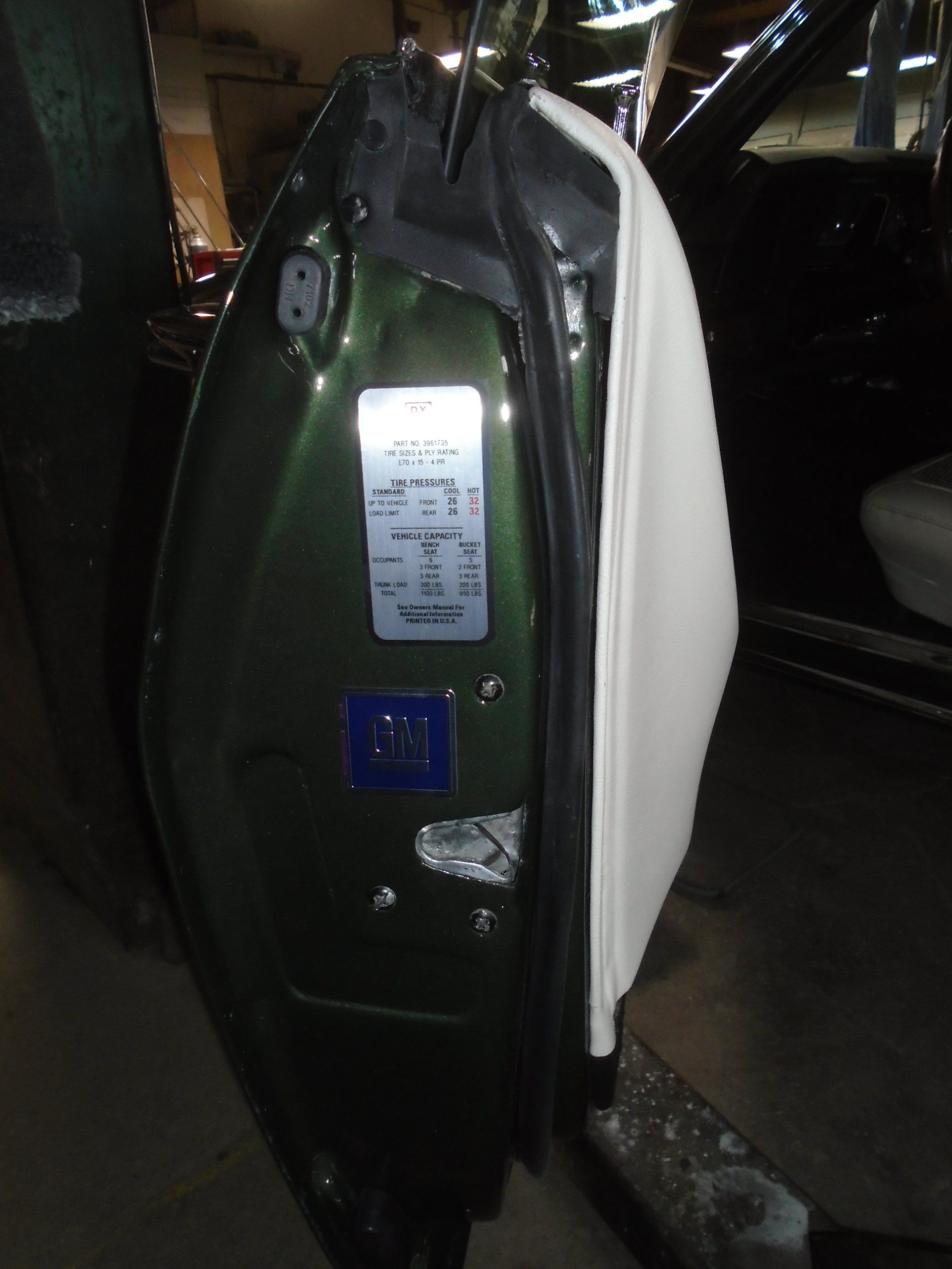 Green car door open, showing white interior, with a vehicle information sticker.