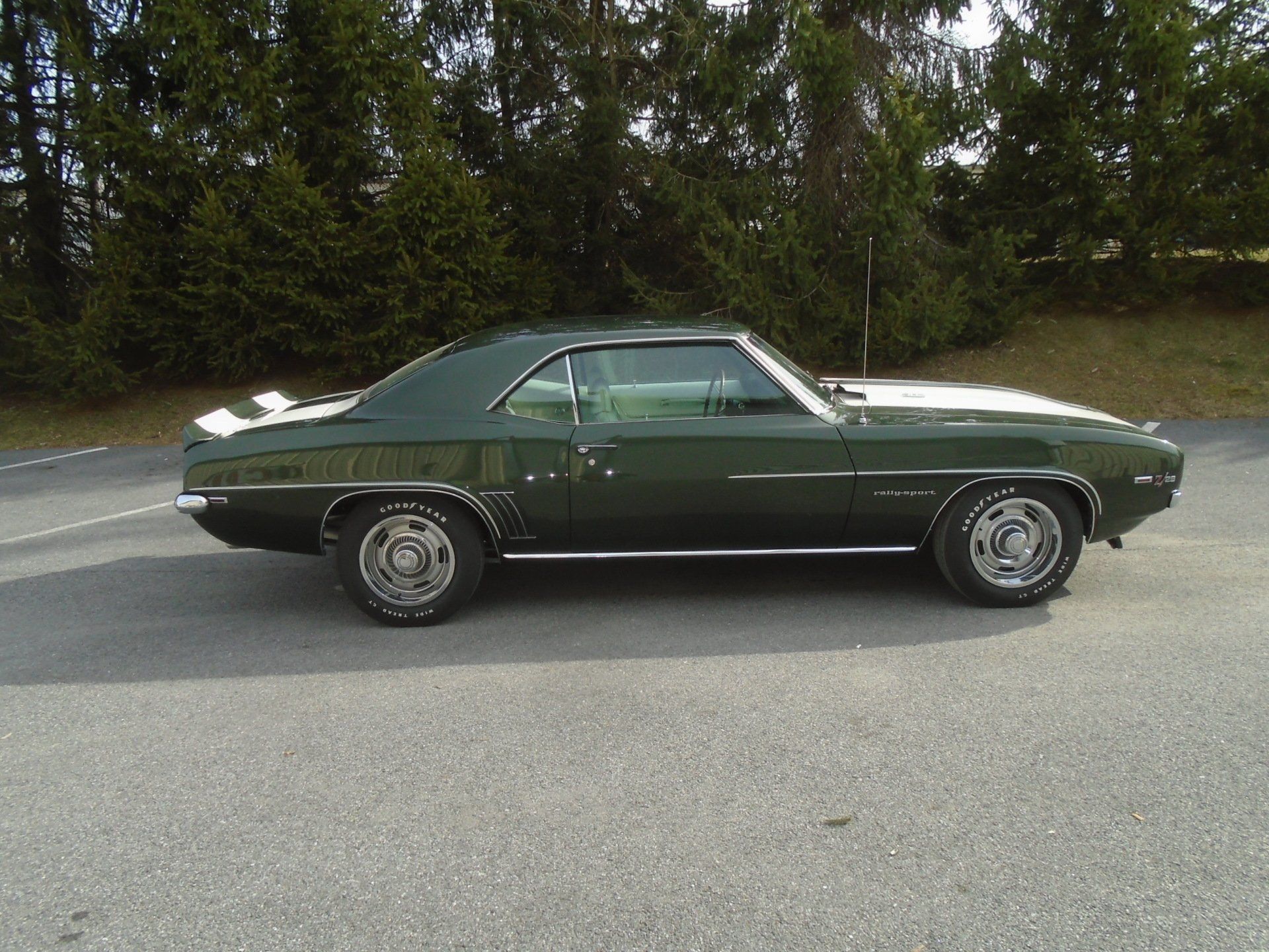 Green classic Chevrolet Camaro with white racing stripe parked on asphalt.