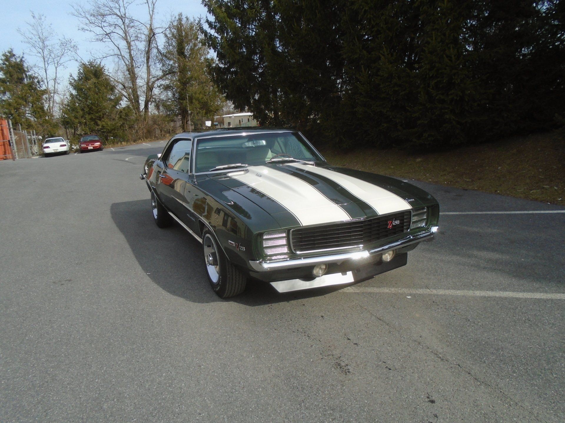 Dark green 1969 Chevrolet Camaro with white racing stripes parked on asphalt.