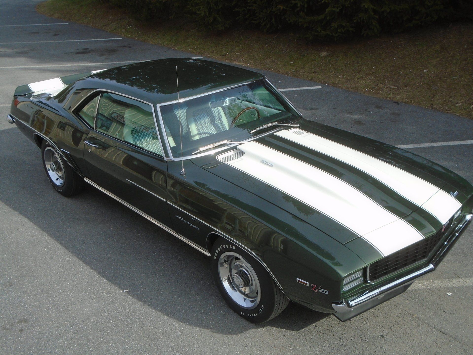 Green 1969 Chevrolet Camaro with white racing stripes parked on asphalt.