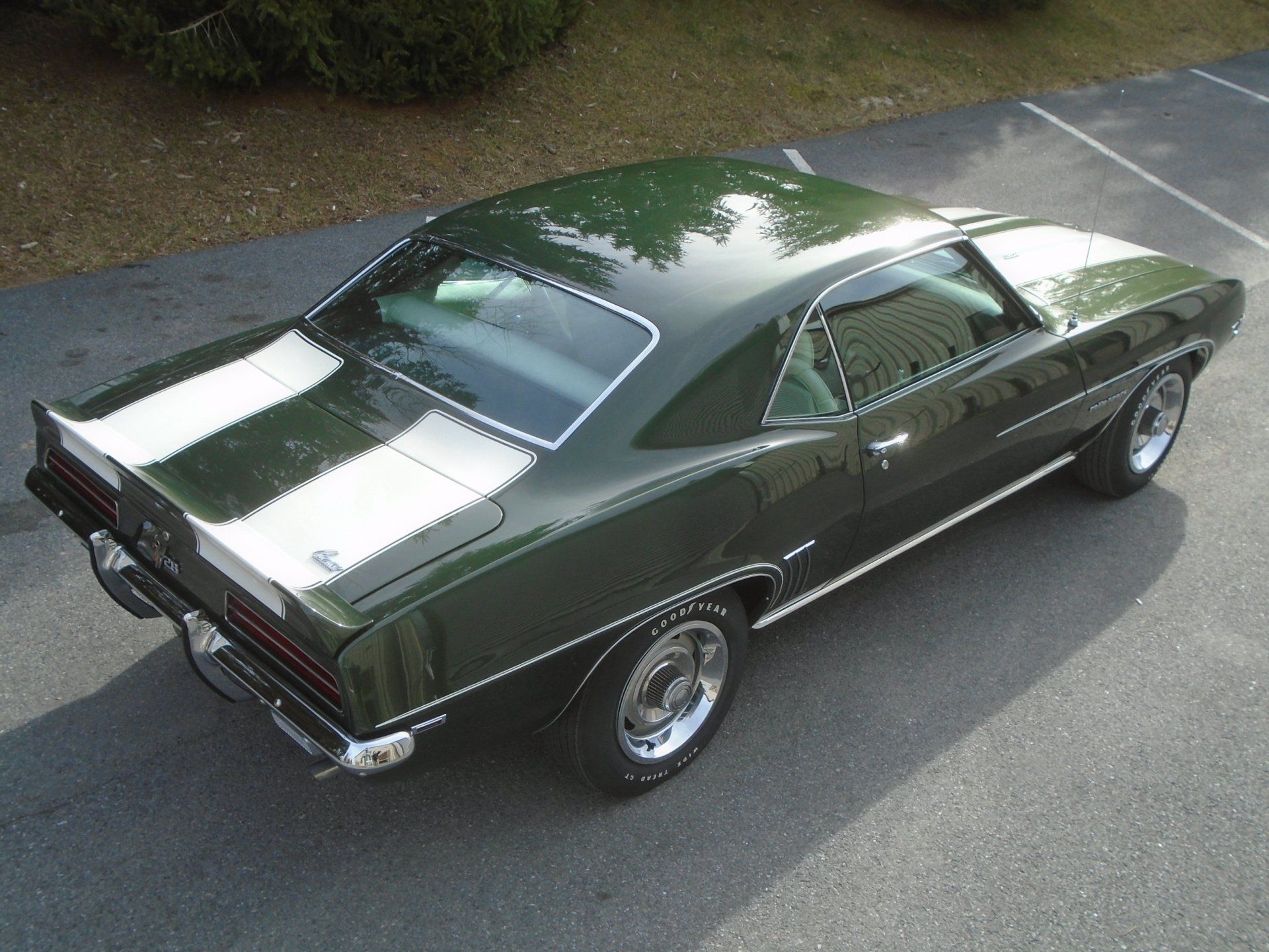 Dark green classic car with white racing stripes, parked on asphalt.
