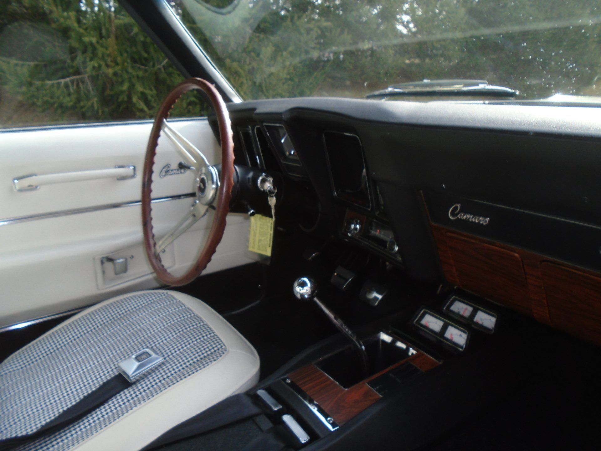 Interior view of a classic black and white Camaro, showing steering wheel, seats, and dashboard.