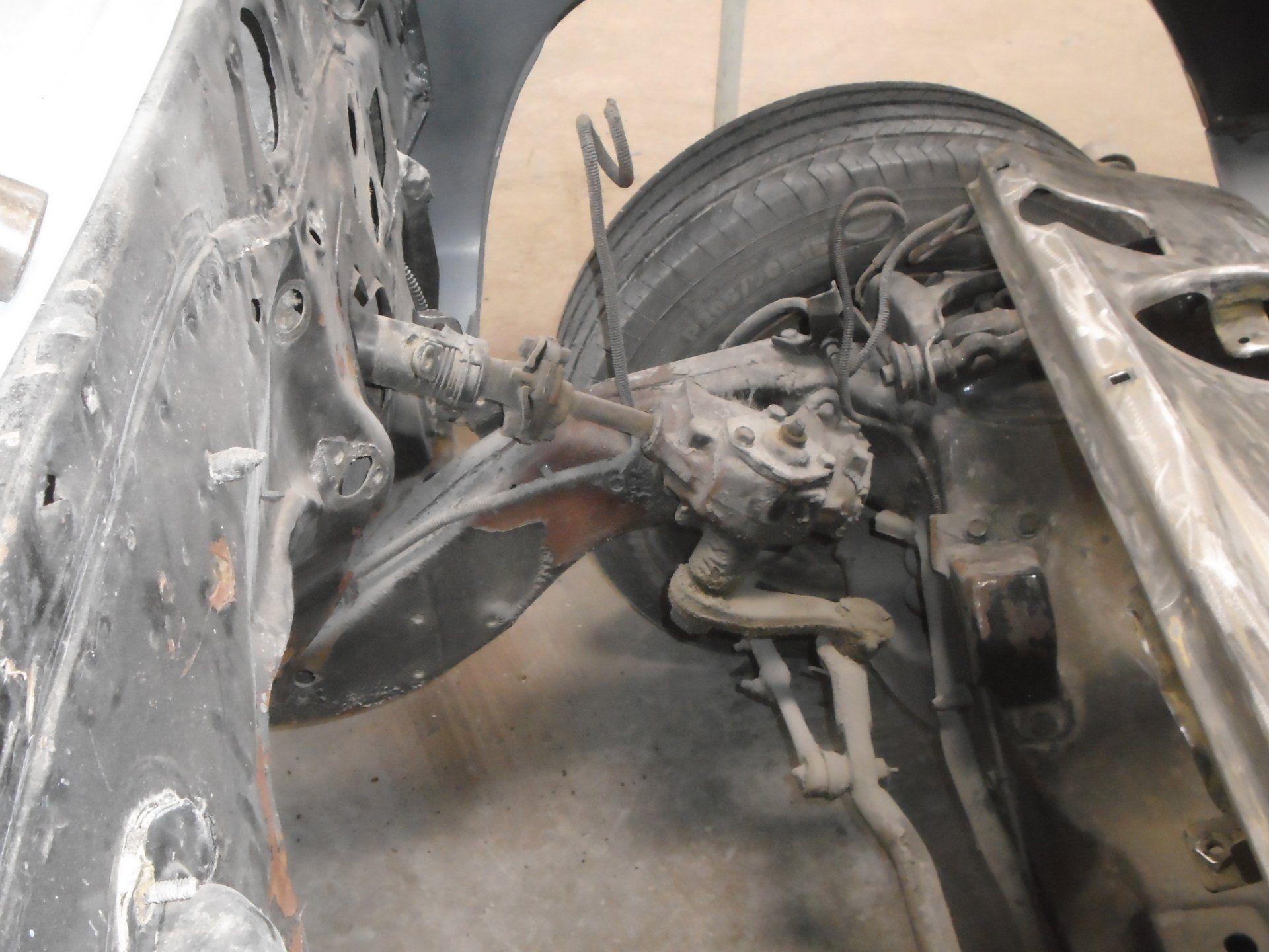Car chassis with front suspension and tire. Black and gray, indoor setting.