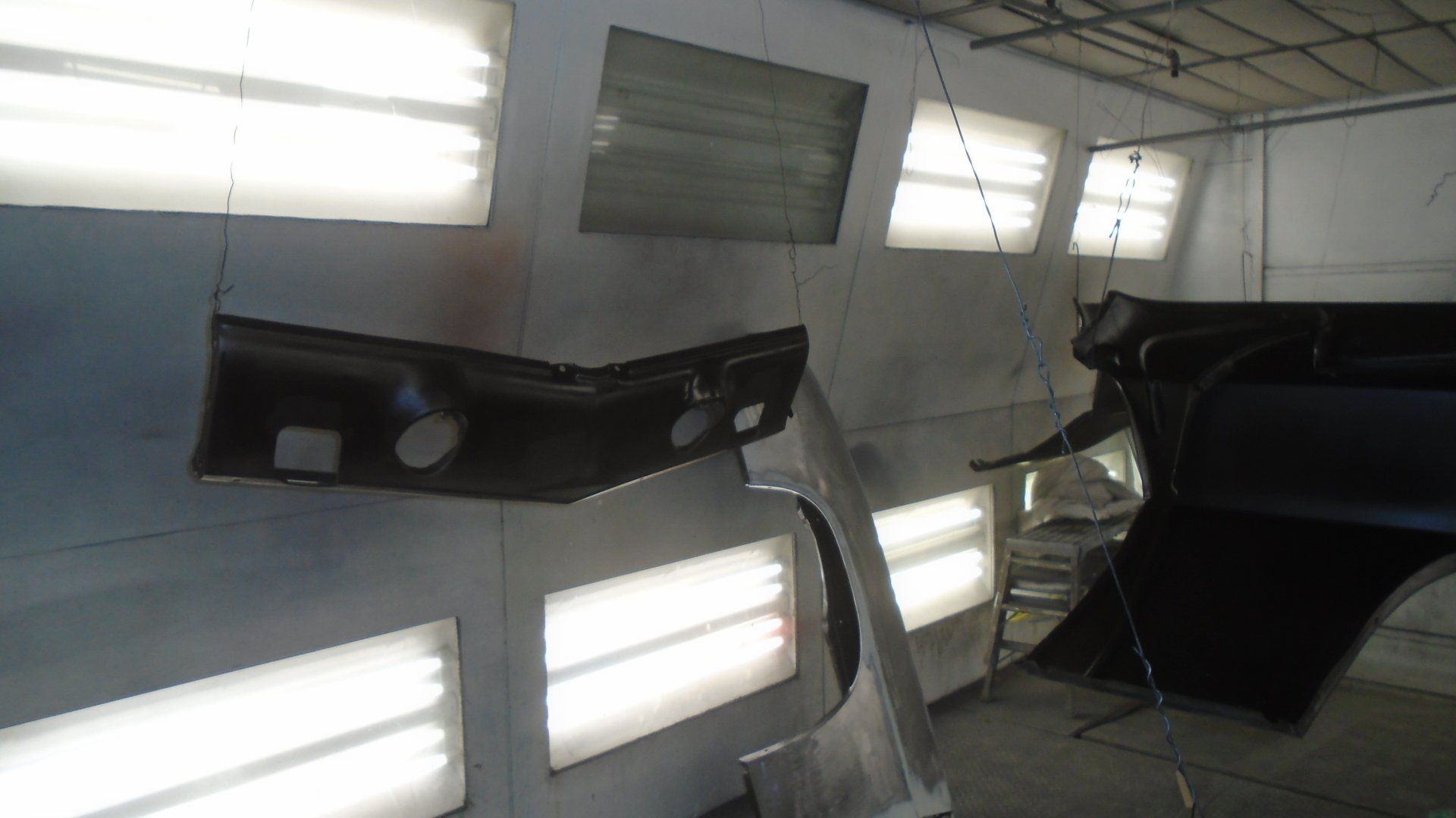Car parts hanging in a spray paint booth with bright lights.