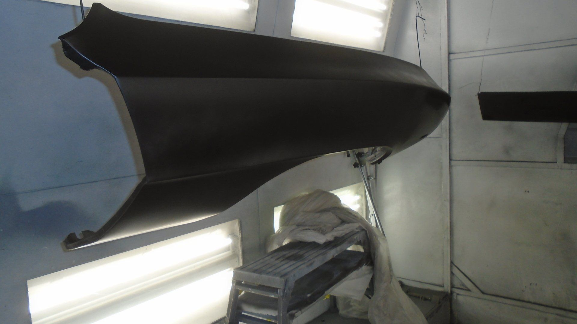 Black car fender being painted inside a spray booth.