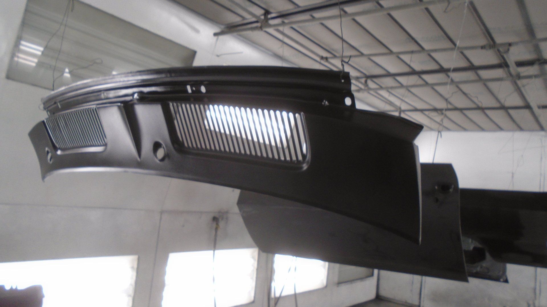 Black car part, likely a dashboard component, hanging in a workshop, freshly painted.