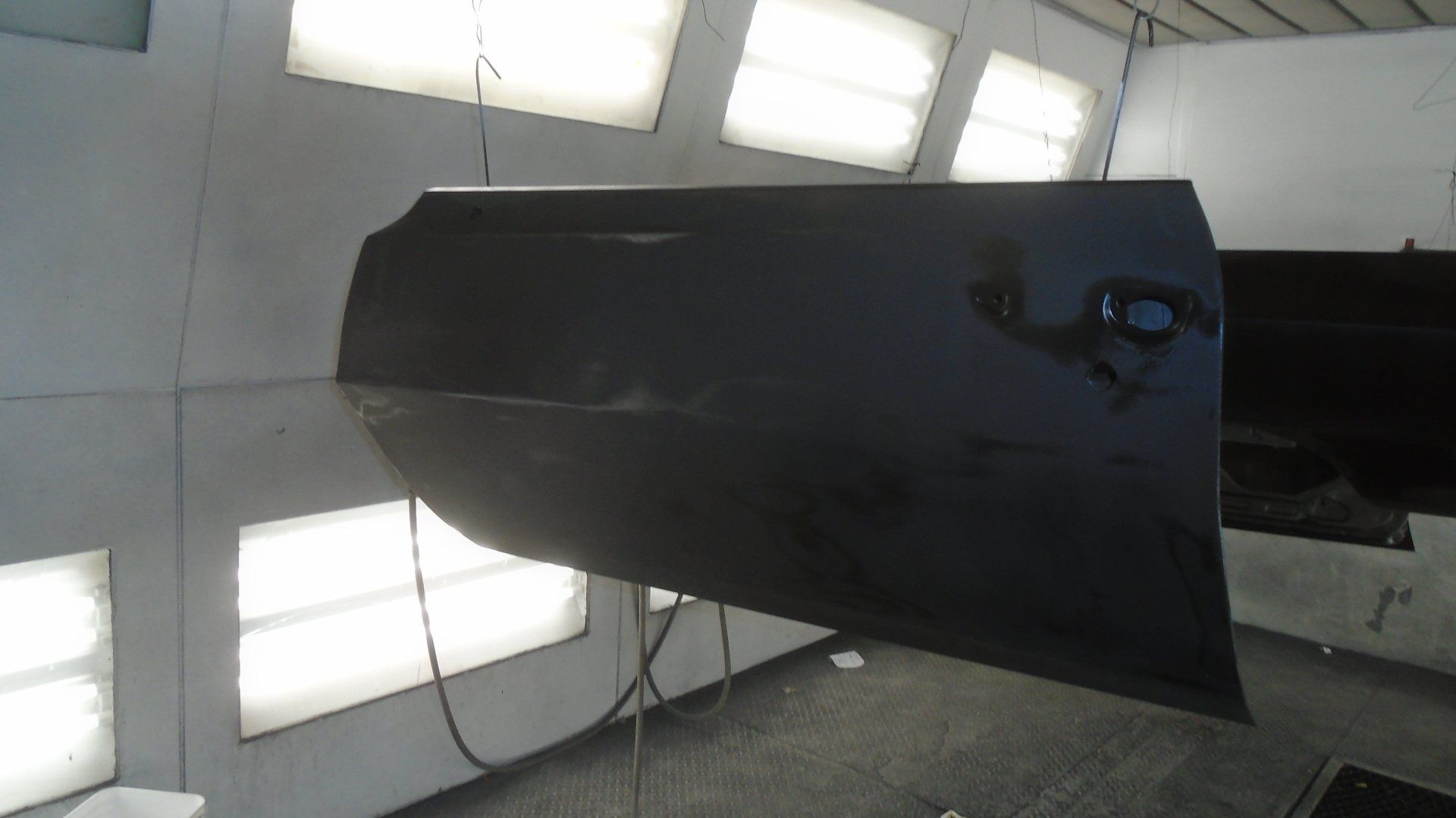 Car door, dark grey paint, hanging in a spray booth.