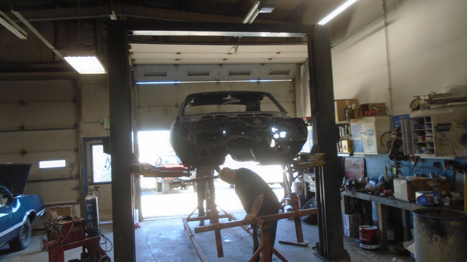 A car chassis raised on a lift in a garage, a person is working underneath it.
