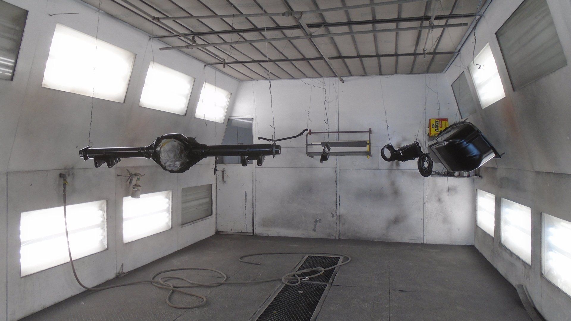 A black car chassis and other parts hanging in a spray paint booth with bright lights.