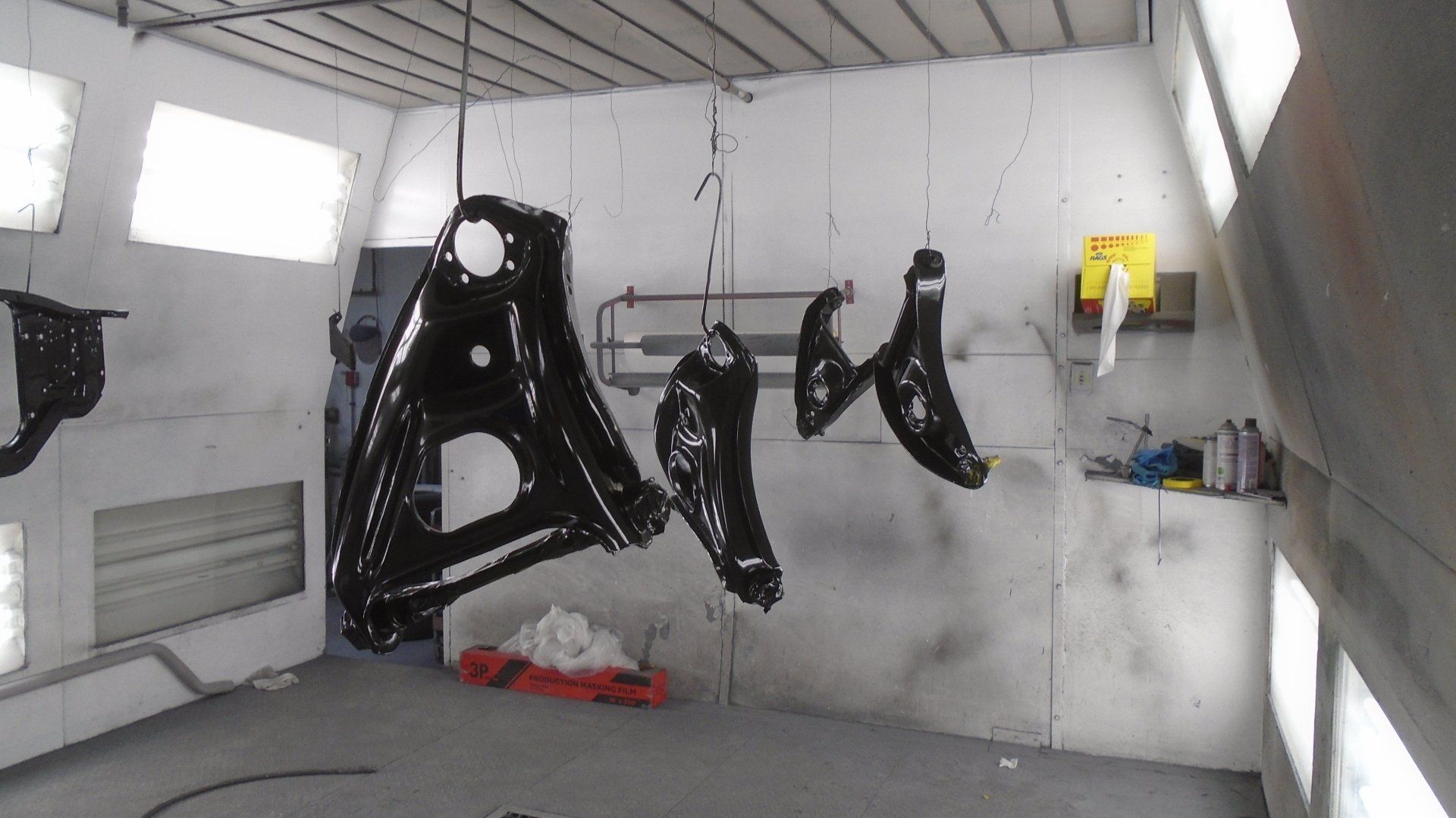 Black vehicle parts hanging in a spray paint booth, ready to dry.