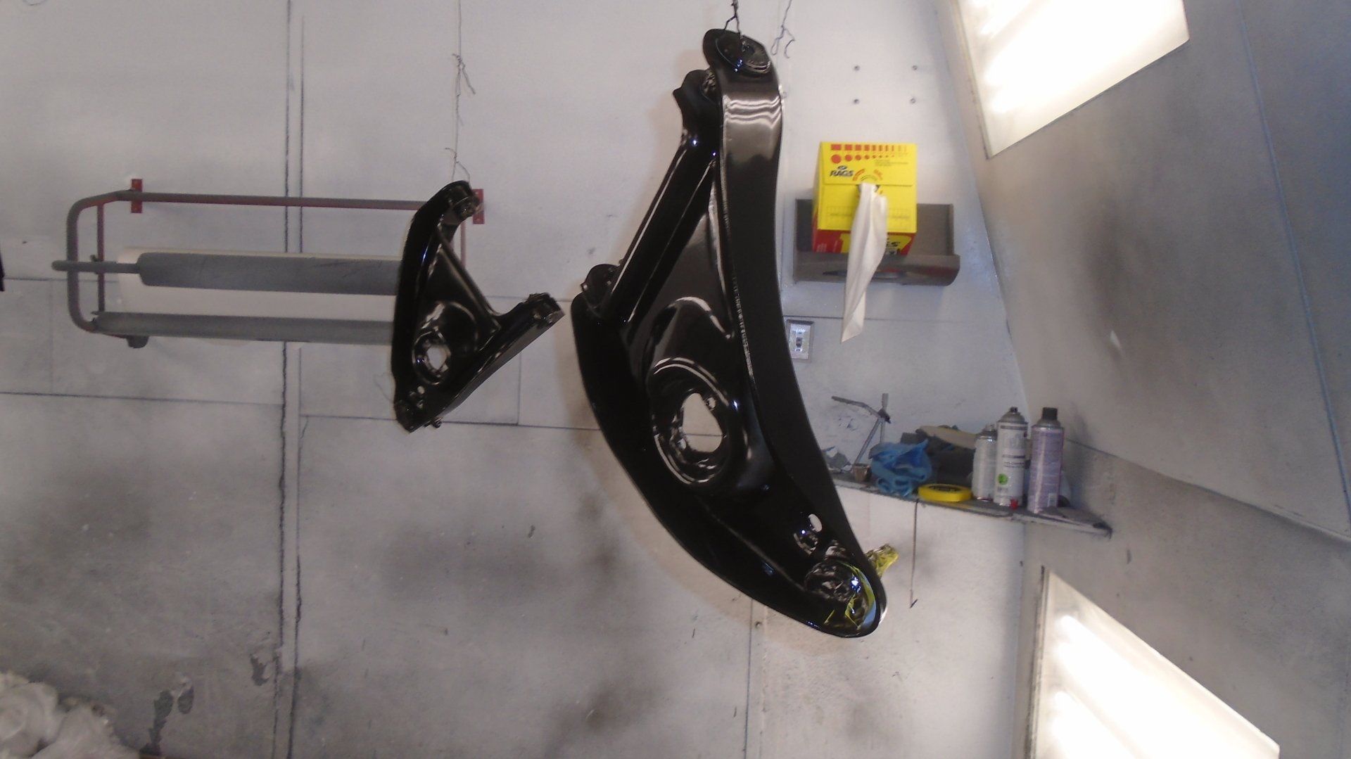 Two black car suspension parts hanging in a spray paint booth.