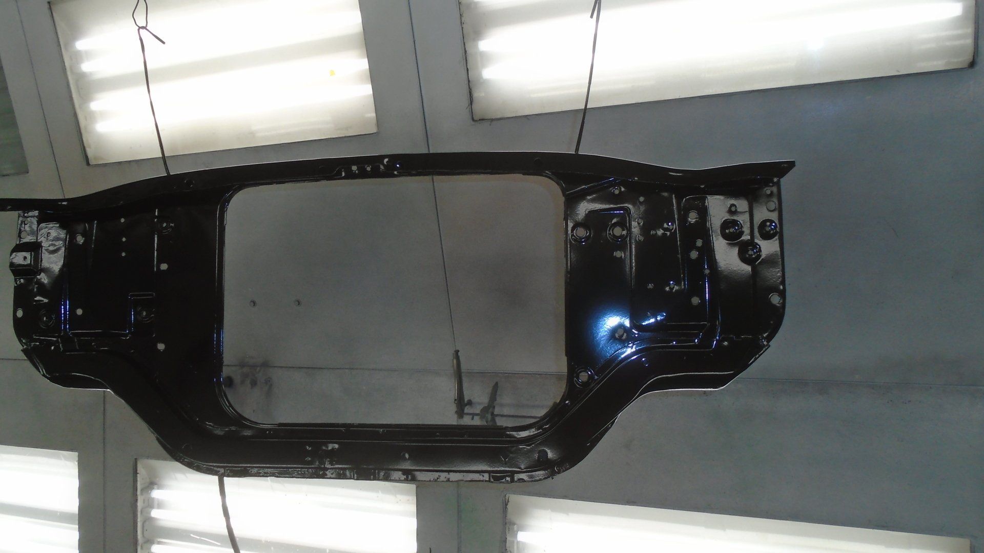 Black car radiator support hanging in a paint booth.