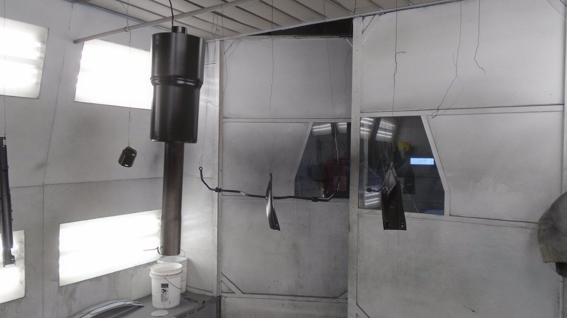 Metal parts suspended in a paint booth, including a muffler and other components, appear freshly painted.