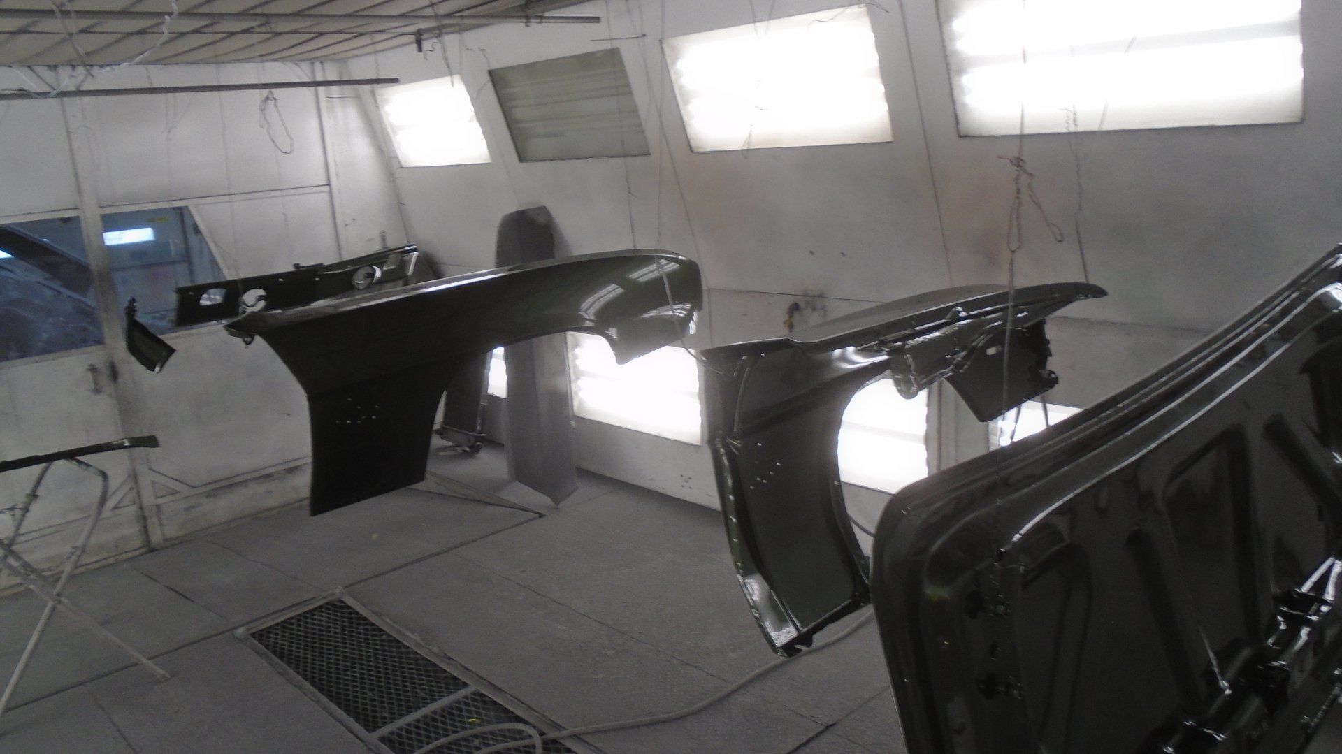 Car parts, likely fenders and doors, are hung in a paint booth for painting, likely black.