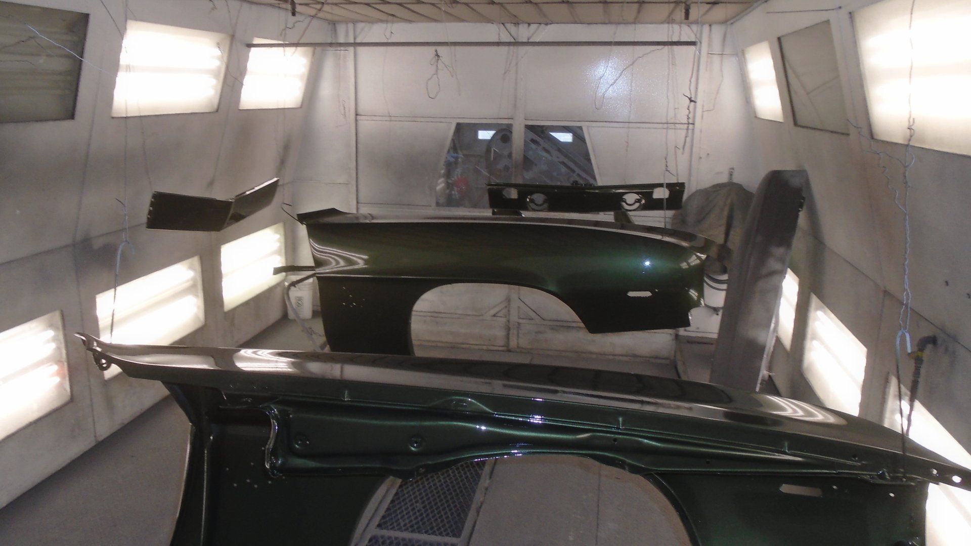 Car parts in a paint booth, freshly painted green.