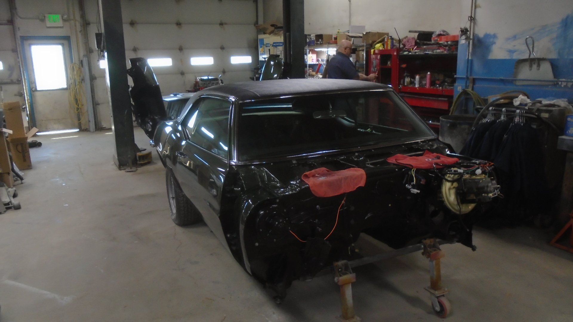 Black classic car body in auto shop, doors open, front end disassembled, ready for restoration.