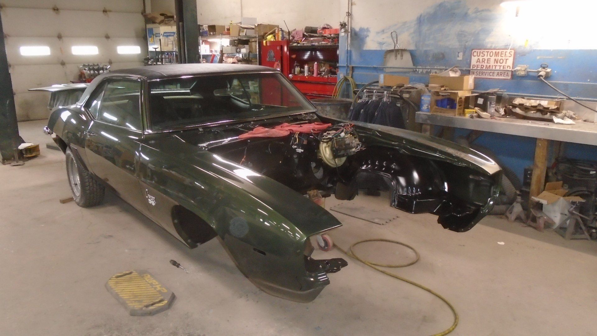 Green classic car in a repair shop; front fenders removed.