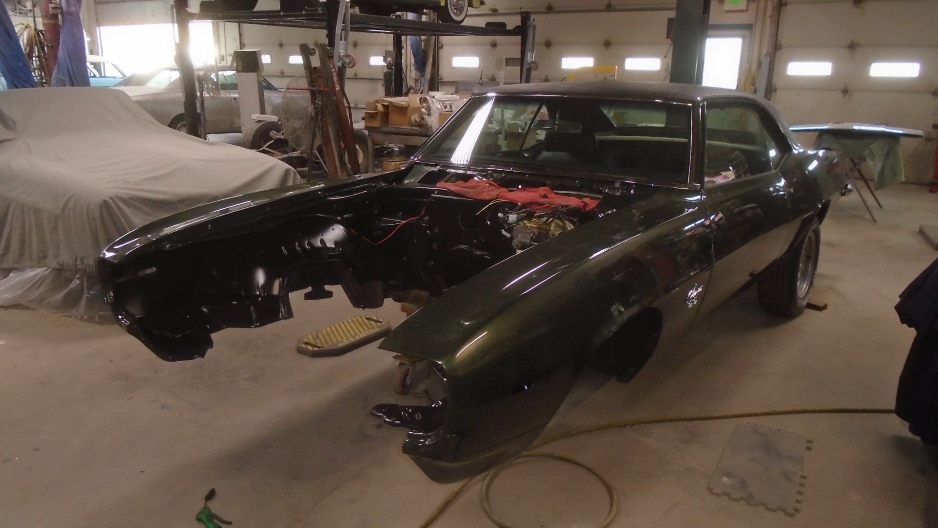 Black classic car undergoing restoration in a garage, missing front end components.