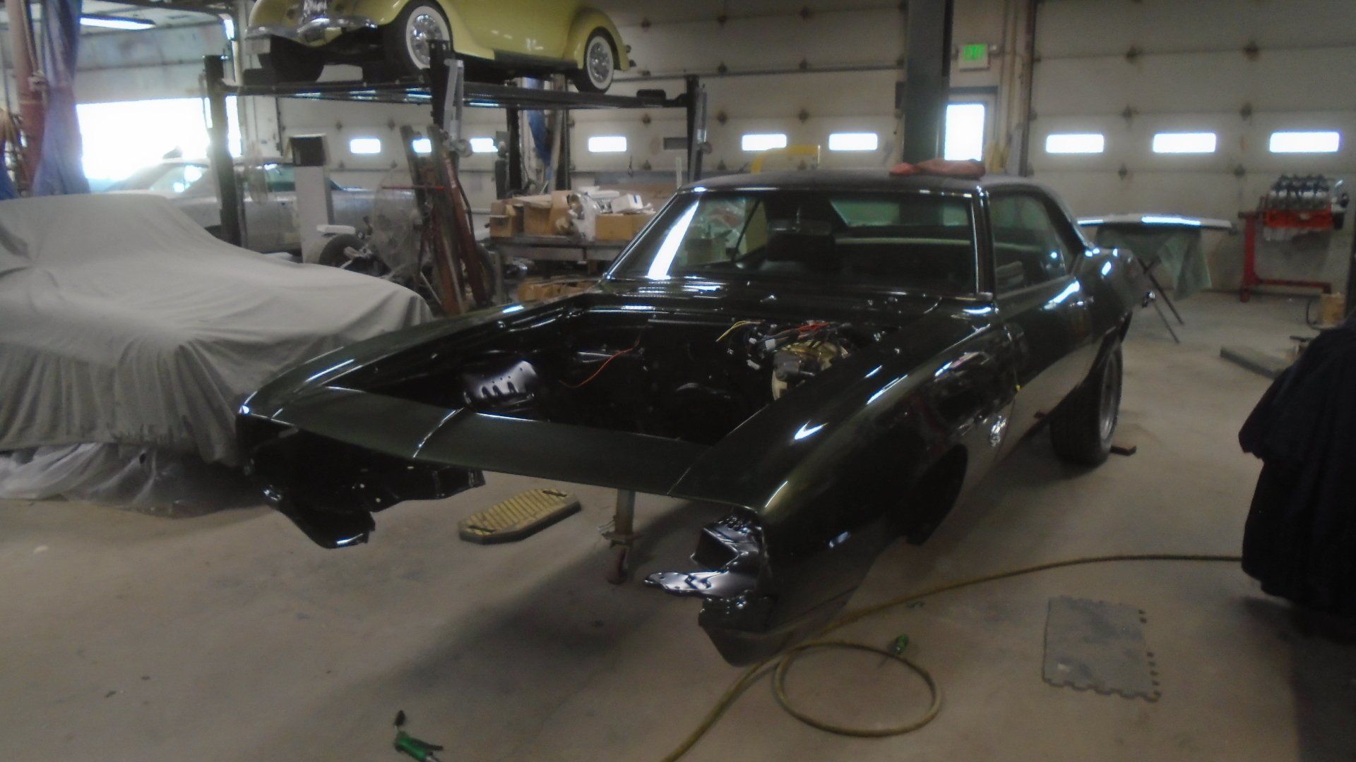 Black classic car in a garage with open hood, undergoing restoration.