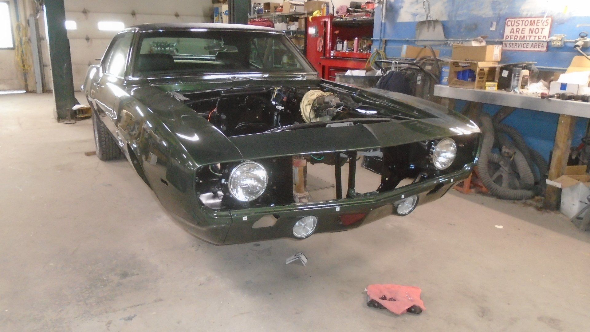 Green classic car in a garage with the hood open, revealing the engine.