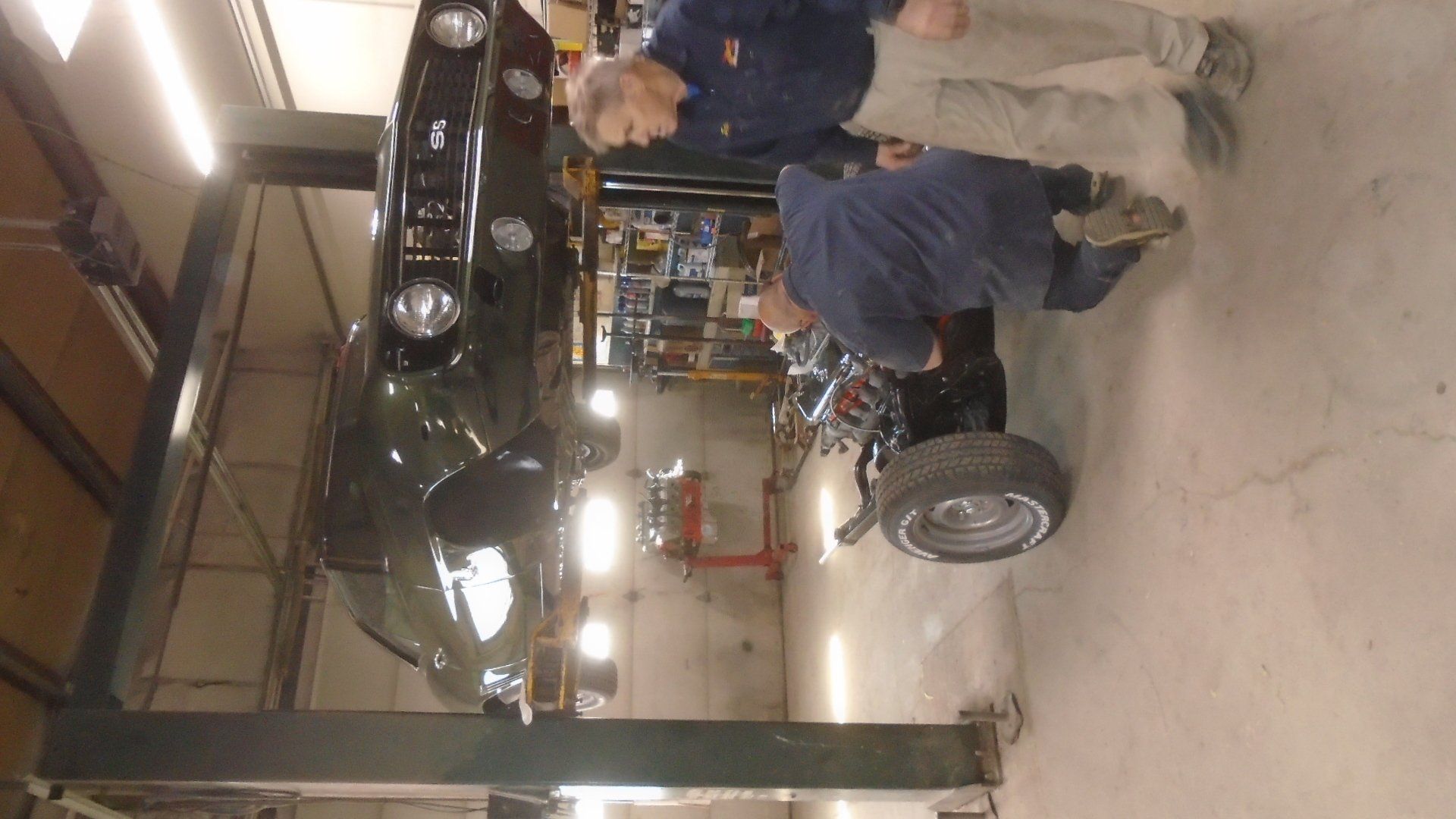 Two men working on a classic car raised on a lift inside a garage.