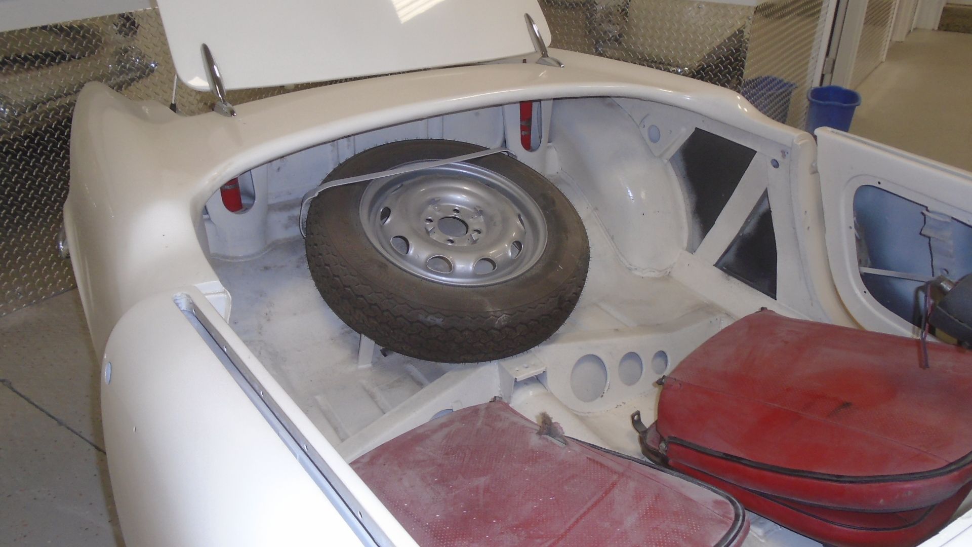Open white car trunk with a spare tire, red container, and other compartments.