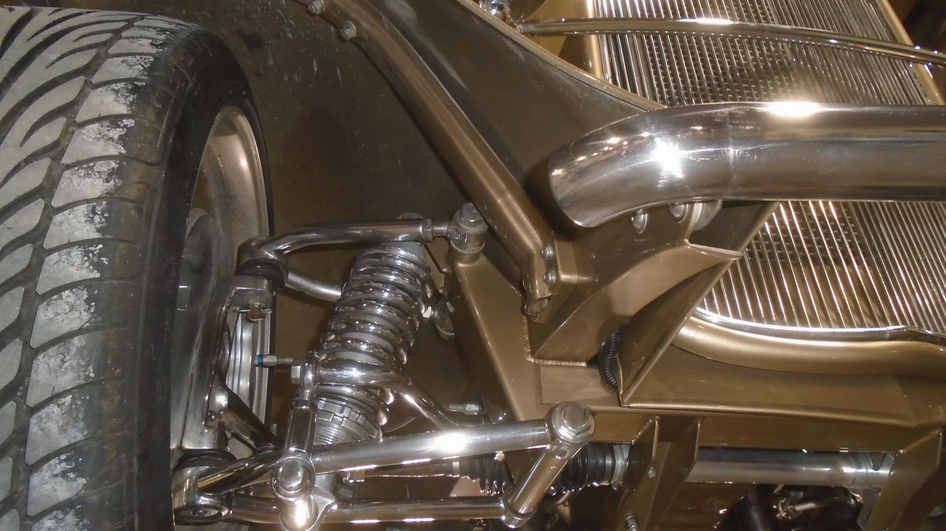 Close-up of a vintage vehicle's front suspension, with chrome components, large tire, and dark brown body.