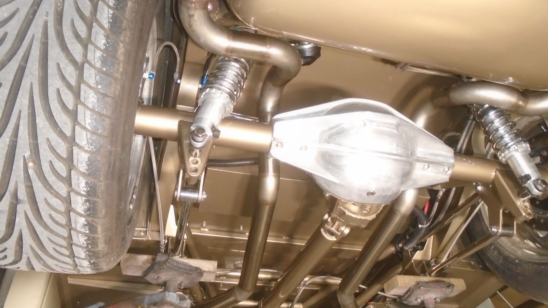 Undercarriage of a custom car, showing the rear axle, exhaust, and suspension components painted gold.