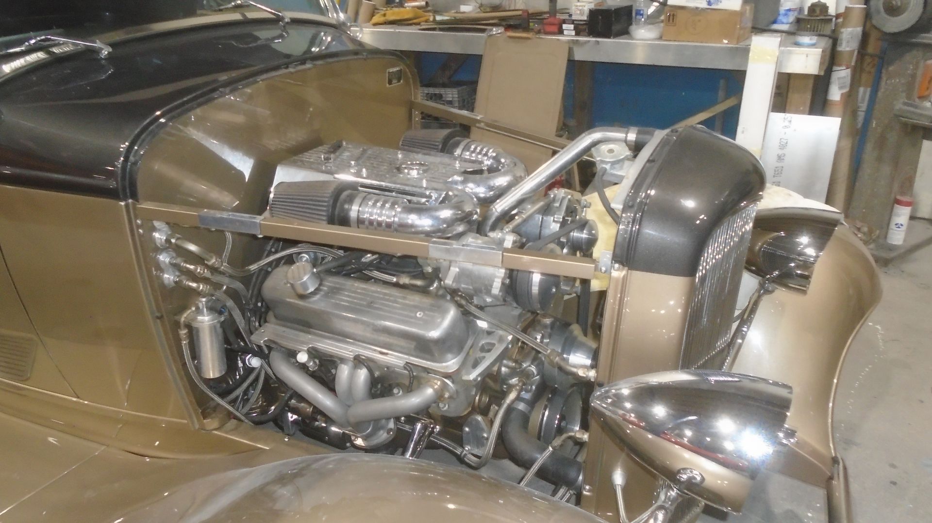 Engine compartment of a classic car, with a large chrome engine and gold body panels.