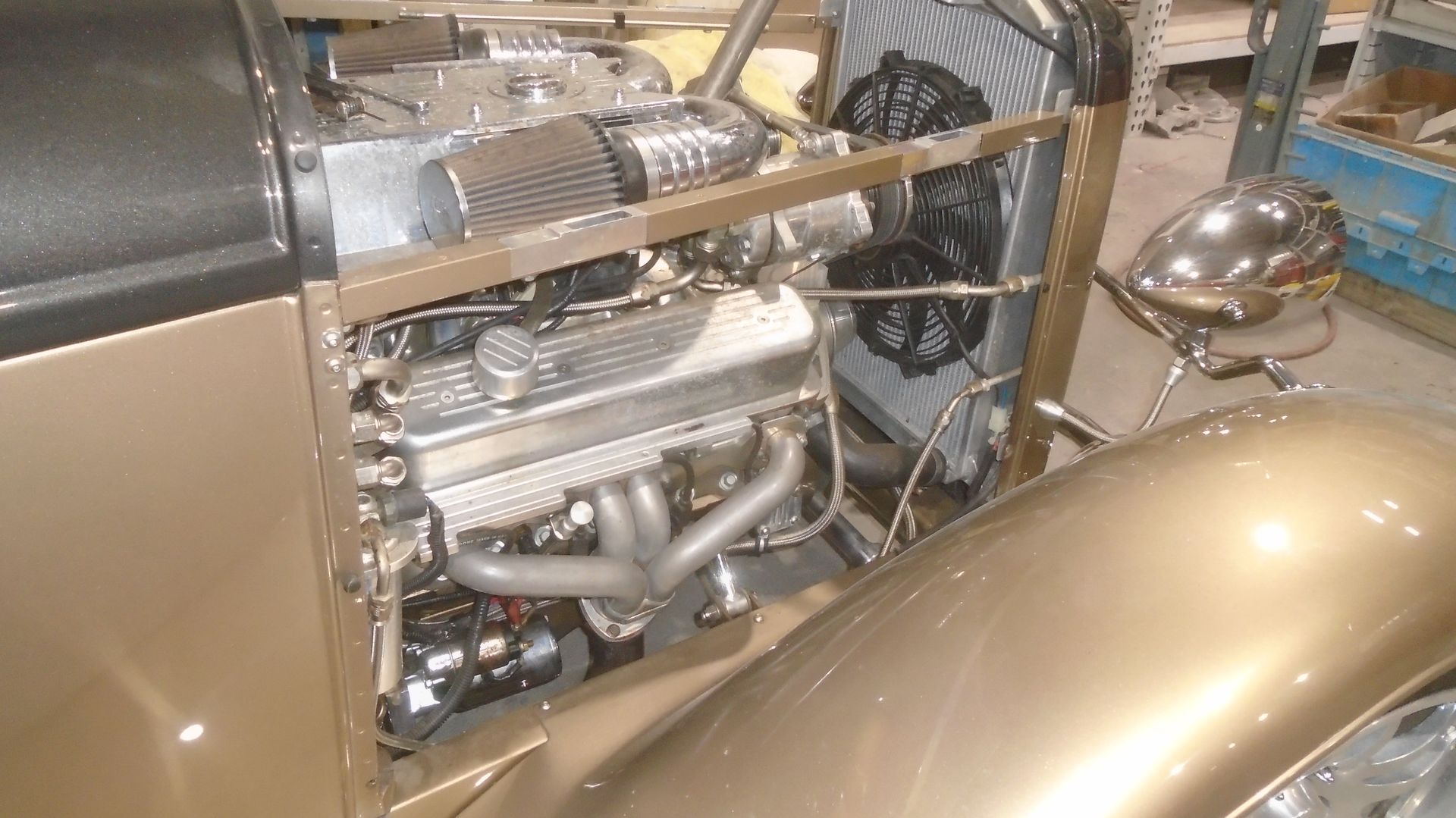Gold hot rod engine bay with chrome details and radiator fan.