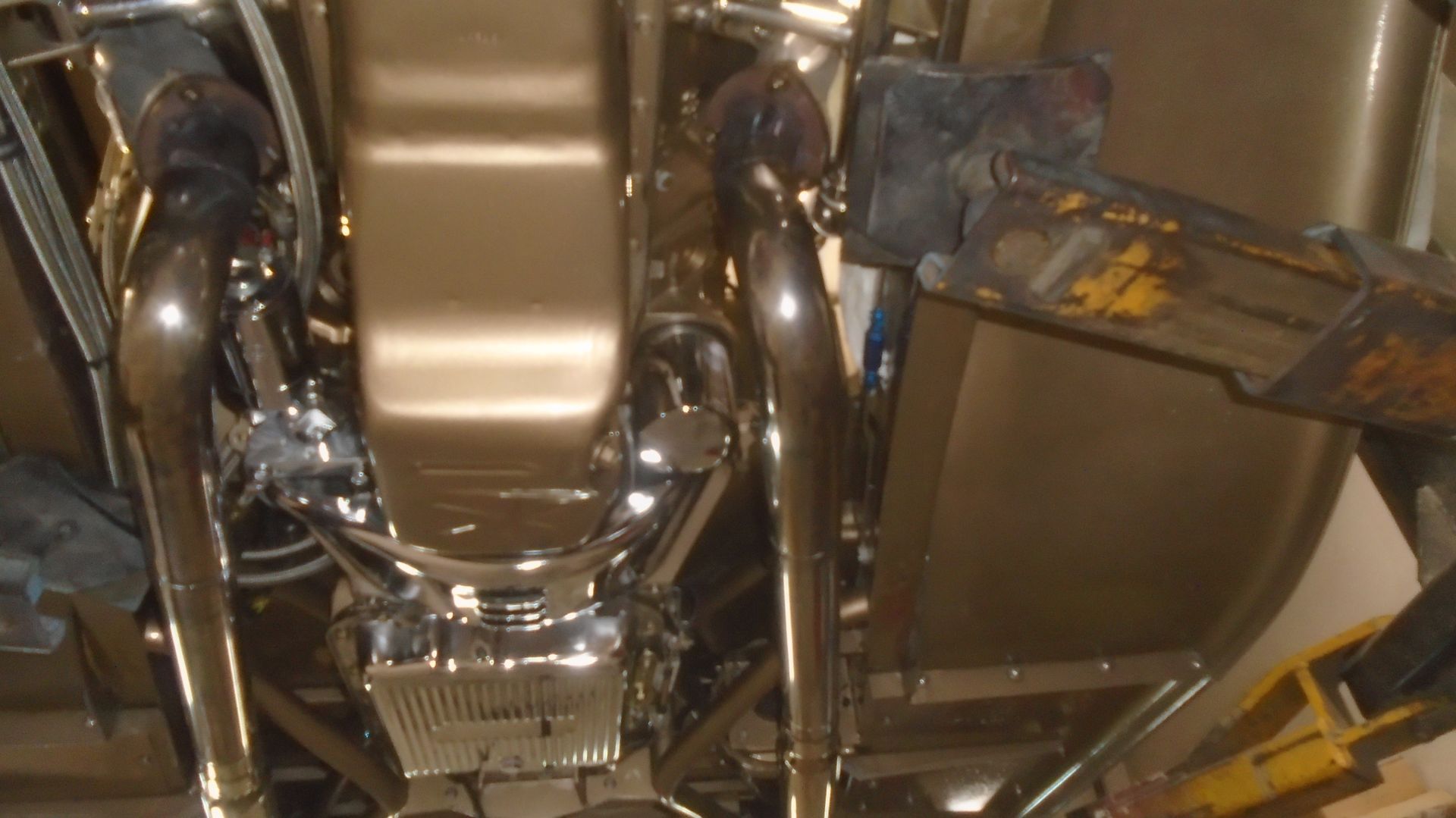 Underside view of a vehicle with shiny chrome exhaust pipes, oil pan, and frame.