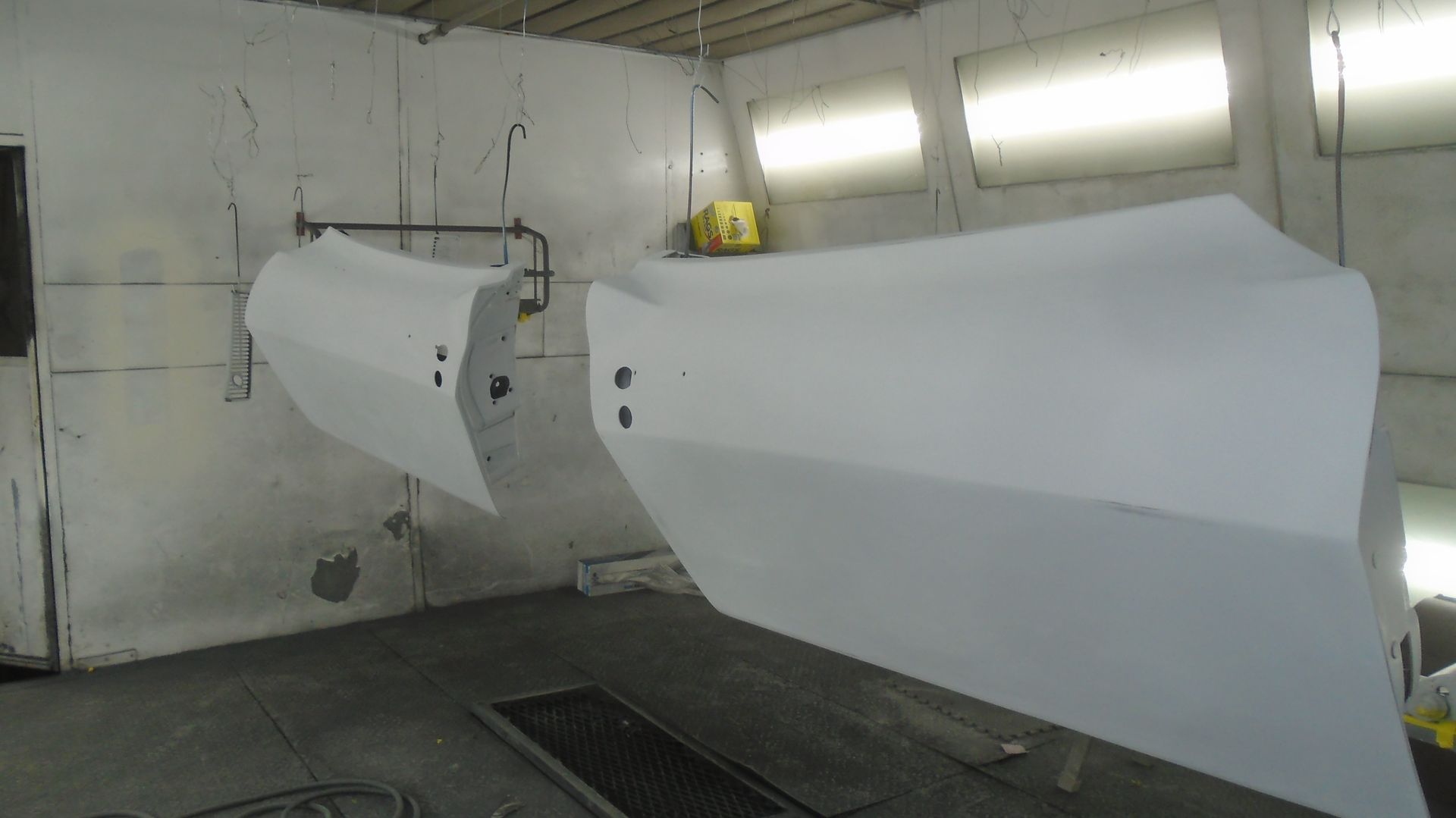 Two car doors, primed white, hanging in a spray paint booth.