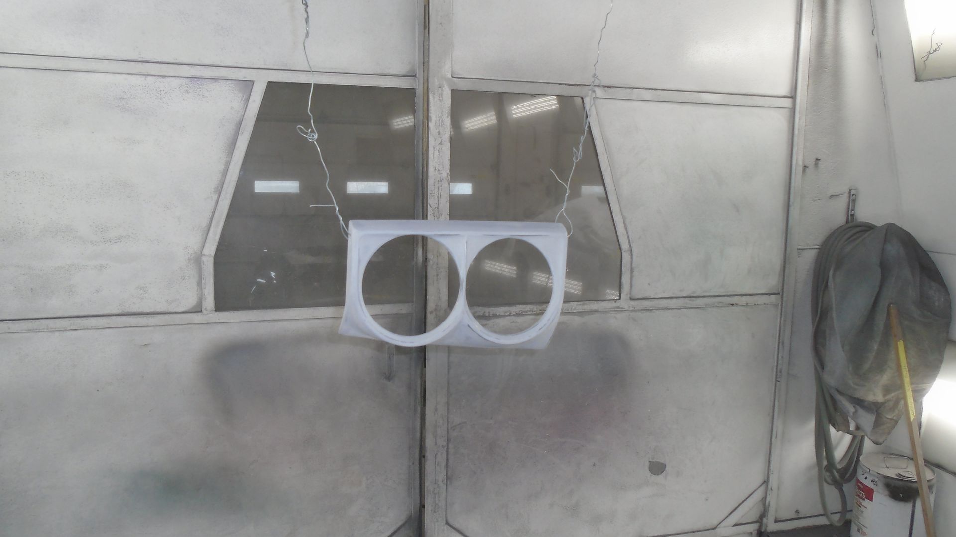 Silver car headlight housing hanging in a spray paint booth.